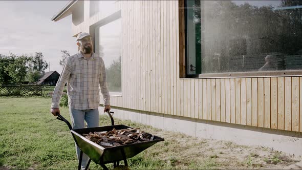 Man is Driving a Wooden Bark on a Wheelbarrow at the Backyard on a Sunny Day