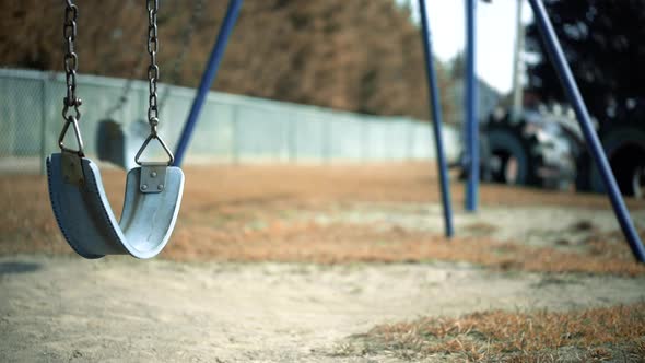 Abandoned Empty Swing Set Swings Swaying In Wind at Children's Playground with Fenceline in backgrou