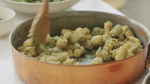 Crop cook adding pesto sauce in pot with pasta