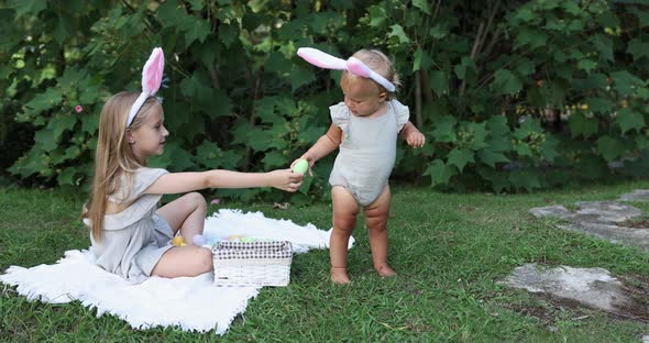 Two Children Wearing Bunny Ears When Pick Up Painted Easter Egg Hunt In Garden or Park