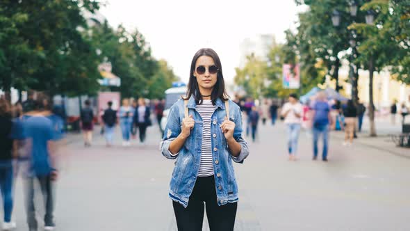 Zoom Out Time-lapse of Confident Young Lady in Sunglasses Looking at Camera Standing in Busy