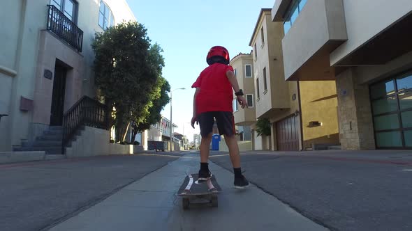 A boy rides a skateboard in a neighborhood alley street.