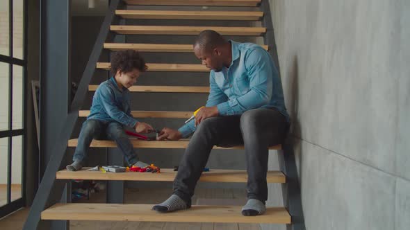 Cute Kid with Dad Playing with Toy Tools on Stairs