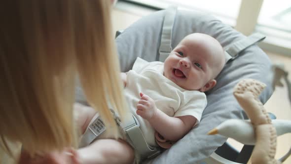 Mother Moving Infant's Legs with the Baby Lying Down on Grey Bouncer Chair