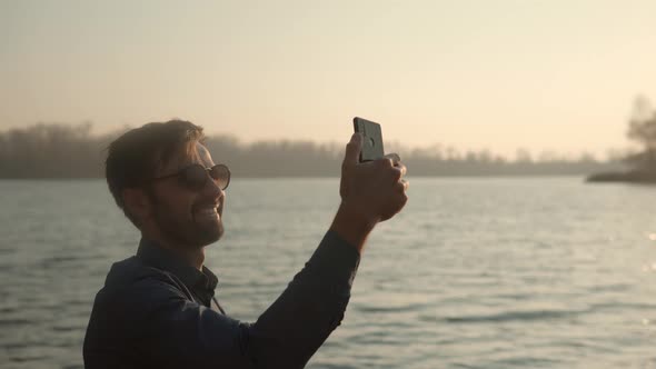 Man Hands Holding Mobile Phone And Taking Picture At Sunset. Guy Taking Photo of Sunset With Mobile.