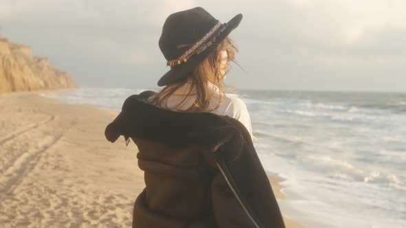 Portrait of Romantic Brunette Woman in Hat and Leather Jacket Walking on the Beach in Autumn at