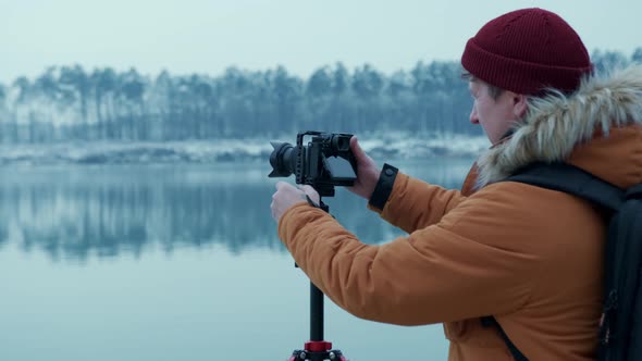 A Male Photographer Adjusts His Camera on a Tripod to Shoot the Edge of a Mountain Forest in the