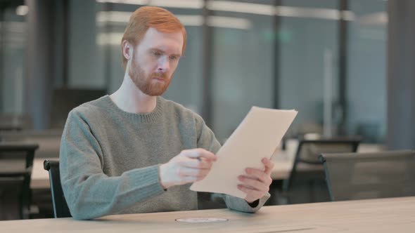 Young Man Reading Reports While Sitting in Office