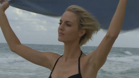 Female wrapping a towel around her on a beach and looking at camera