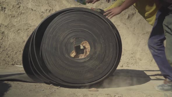 Unrecognizable Factory Workers Rolling Heavy Conveyor Belt Manually. Side View of Caucasian Male