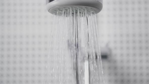 Water Flowing From Shower Head in Bathroom, White Tiles Black Pattern on Walls, Drops in Slow Motion