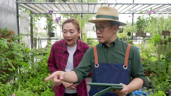 4K Asian man plant shop owner teaching woman employee caring plants and flowers