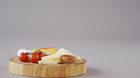 Different types of cheese, tomatoes and bowl of jam on wooden board
