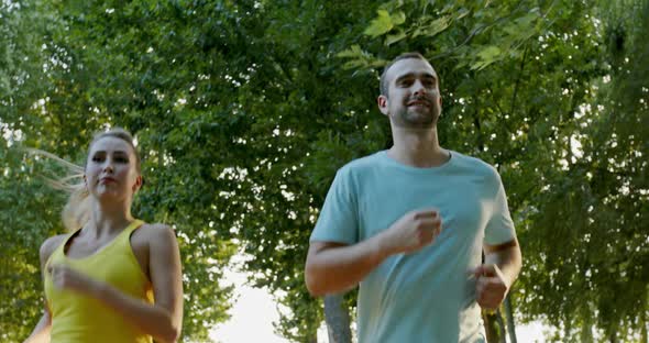 Couple of Athletes Running in Park, Low Angle Tracking Shot of Happy Sportsman and Sportswoman