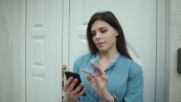 women with brunette hair in denim overalls Smiling and positive using and texting on her phone