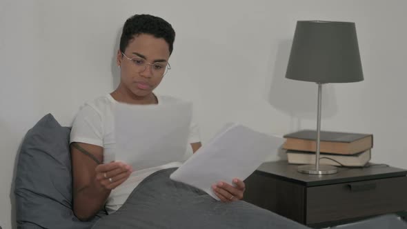 African Woman Reading Documents While Sitting in Bed