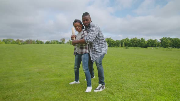 Positive Black Father and Son Practicing a Bat Swing Outdoors