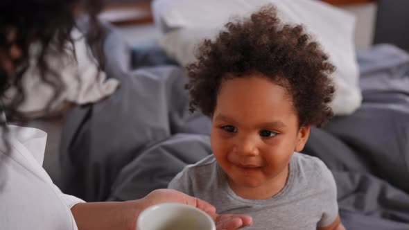 Portrait of Charming African American Toddler Drinking Healthful Juice As Woman Feeding Child