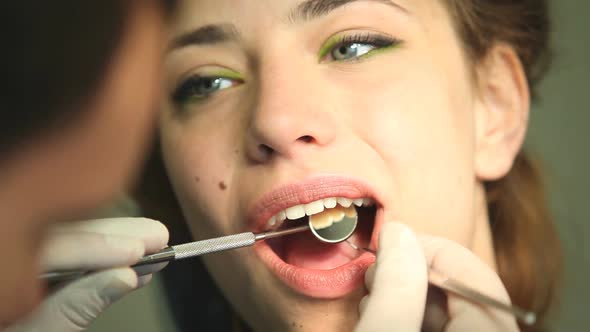 Close up of girl keeping mouth open while dental assistant examining her teeth