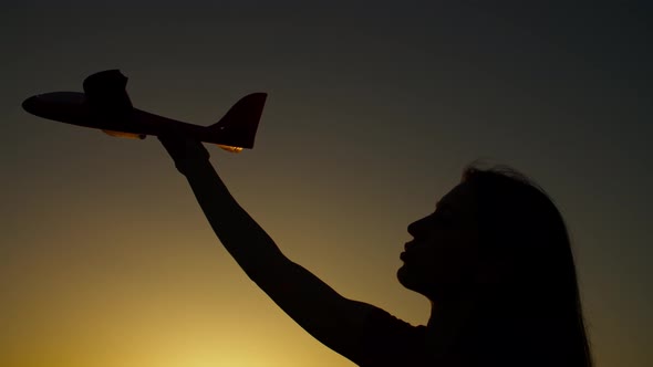 Silhouette of Female Hand with Toy Airplane at Sunset