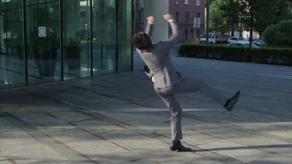 Super Slow Time Young Businessman Makes a Difficult Jump in Front of the Business Center Rejoicing