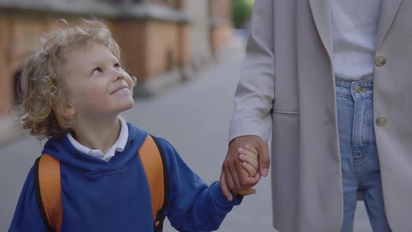 Son Looking at His Mother and Holding Her Hand Smilling on the Road to School