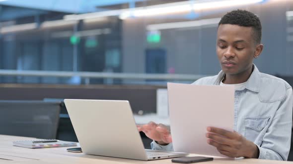 Man with Laptop Reading Documents in Office