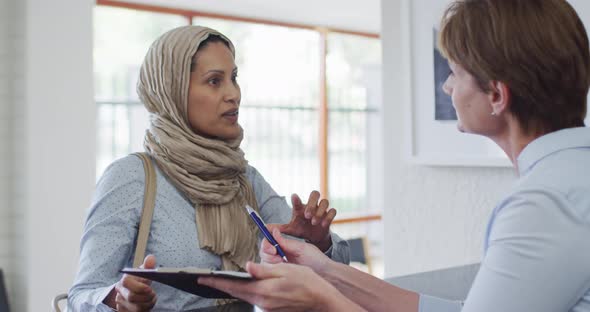 Smiling biracial woman talking and signing documents at reception at modern dental clinic