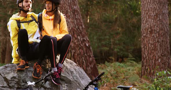 Mountain biking couple sitting on a rock in the forest