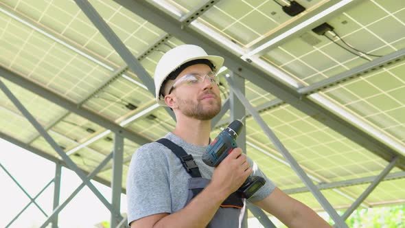 Male Engineer in Protective Helmet Installing Solar Photovoltaic Panel System Using Screwdriver