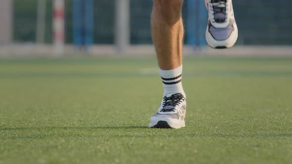 Closeup Swarthy Tanned Male Legs in Sports White Sneakers and Socks on Grass of Stadium