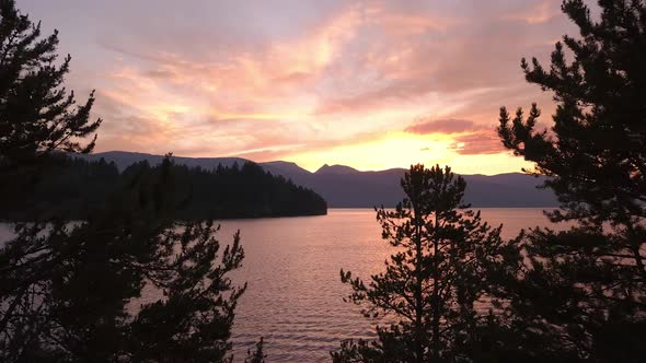 Aerial view flying through trees over lake with colorful sunset