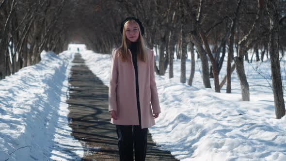 Fashionable Blonde Model in Pink Coat and Black Beret Posing Among Bare Trees Outdoors in Winter