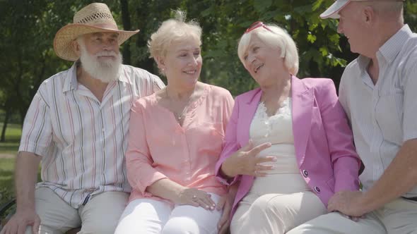 Two Cute Mature Couples Talking and Smiling Sitting on the Bench in the Summer Park