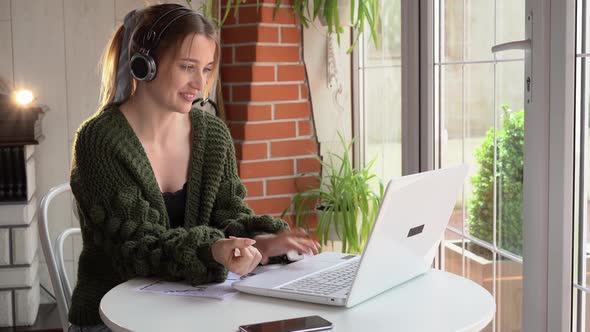 A Beautiful Freelance Woman Works on the Line with a Headset with a Microphone and Looks Into a