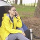 Young woman tourist sitting near a tent and talking on smart phone in forest. - VideoHive Item for Sale