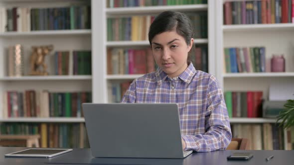 Indian Woman Smiling at Camera while using Laptop in Office