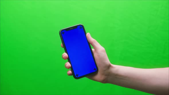 Closeup of Smartphone with Blue Screen Young Man Hands Holding Mobile Phone on Green Background