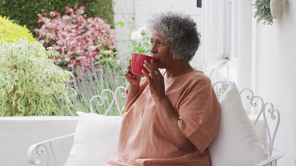 Senior african american woman drinking coffee while sitting on the porch of the house