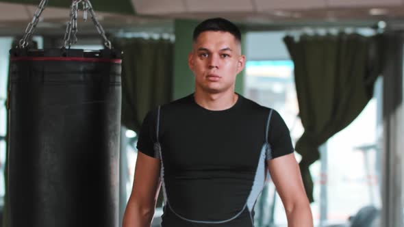 Young Man Boxer Passing By the Punching Bag and Stands in the Protective Stance