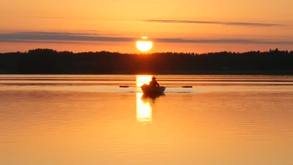 Silhouette of Man Rowing on Boat in Reflection of Golden Sunset Over Lake