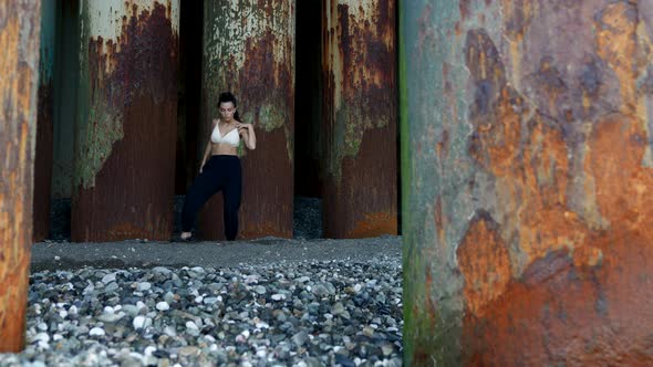 Modern Dance Under Pier on Sea Shore Young Woman is Dancing Near Old Rusty Supports