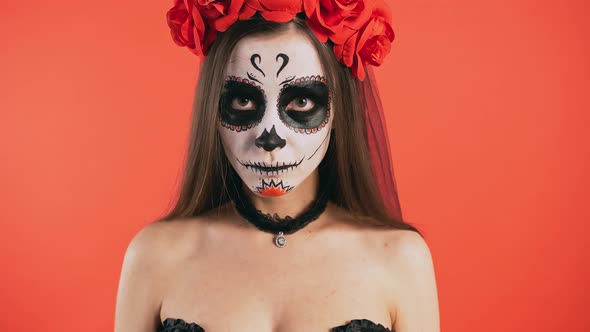 Day of Dead Woman with Sugar Skull Makeup is Staring at you By a Creepy Look Posing on Red