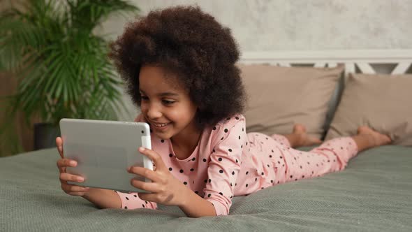 Cute Little African American Girl in Plays a Game on a Digital Tablet and Rejoices at the Victory