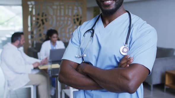 Portrait of african american male doctor smiling, with colleagues in discussion in background