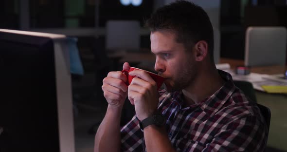 Businessman drinking coffee and working in a modern office by night