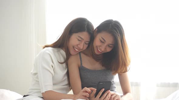 young asian women LGBT lesbian happy couple sitting on bed hug and using phone