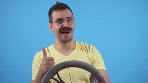 Funny Man with Moustache at the Wheel Shows a Thumbs Up on a Blue Background of Slow Mo Isolate