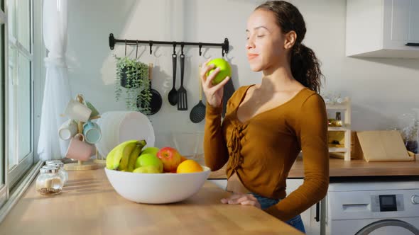 Young attractive Latino woman eat fruits on table in kitchen at home.