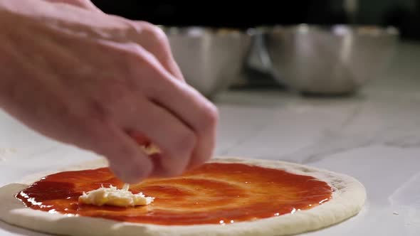 Baker prepares traditional Italian pizza. cook puts pieces of cheese on dough